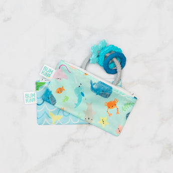 Bumkins Silicone Teething Charms: Blue peeks out of two stacked ocean-themed pouches on a marble background.