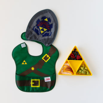 Bumkins Caped SuperBib®: The Legend of Zelda™ Link lays flat next to a yellow triangle-shaped plate with fruit on a white background.