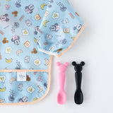 Bumkins Silicone Dipping Spoons: Minnie Mouse (Black and Pink) sit next to a blue sleeved bib with breakfast pattern on a white background.