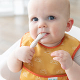A baby wearing a yellow bib chews a Bumkins Silicone Dipping Spoons 3 Pack: Rocky Road while seated in a high chair.