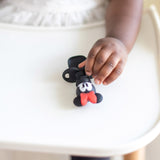 A young child in a white shirt holds a Bumkins Silicone Chewtensils®: Minnie Mouse.