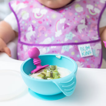 Baby enjoys kiwi in yogurt from a turquoise bowl, using Bumkins Fuchsia Silicone Chewtensils—a safe start for baby-led weaning.