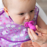 A baby in a vibrant unicorn-themed bib is being fed with a Bumkins Silicone Chewtensils® in Fuchsia, held by an adult. Sitting in a high chair, the baby looks focused on their meal, practicing the baby-led weaning approach.