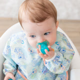 A baby in a pastel bib uses a utensil from Bumkins Grip Dish Deluxe Infant 5-Piece Mealtime Set: Blue Jelly to explore self-feeding.