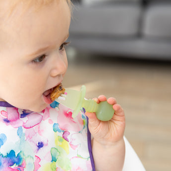 Close-up of a child using a utensil from Bumkins First Foods Essential 5-Piece Mealtime Set: Green Jelly to eat a piece of pancake.