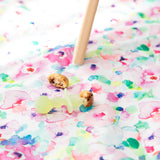 A Bumkins Silicone Chewtensils®: Green Jelly lays on top of a floral mat next to pancake pieces under a high chair leg.