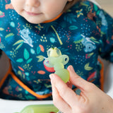 Close-up of an adult hand feeding a child in a dark blue bib with a Bumkins Silicone Chewtensils®: Green Jelly.