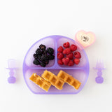 A purple plate with waffles and berries, a heart-shaped yogurt cup, and Bumkins Silicone Chewtensils®: Purple Jelly on a white background.