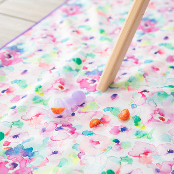 Bumkins Silicone Chewtensils®: Purple Jelly lay on top of a floral play mat next to pieces of tomato.