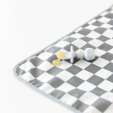 A Bumkins Silicone Chewtensils®: Marble lays atop a gray & white checkered mat on a white background with applesauce on top.