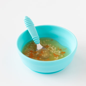 A blue bowl with small pasta, veggies, and Bumkins silicone spoon ensures easy self-feeding for toddlers.