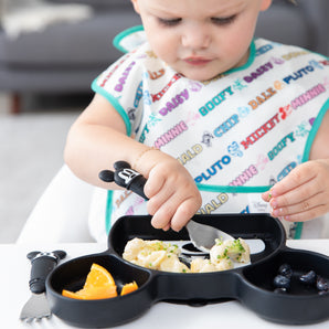 A girl in a Mickey and Friends bib uses Bumkins Spoon + Fork: Mickey Mouse to scoop mac & cheese with broccoli from a Mickey Mouse Grip Dish.