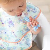 Close-up of a toddler wearing a pastel bib in a high chair with a Bumkins Spoon + Fork: Stitch in their mouth.