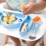 A Bumkins Spoon + Fork: Stitch sits on a high chair tray next to a Stitch-shaped dish with breakfast foods; a child’s hand visible above.