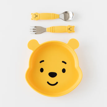 A plate and matching toddler utensils from Bumkins On-The-Go Mealtime 7-Piece Set: Pooh Bear + Friends rest on a white background.