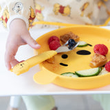 Close-up of a child's hand reaching for a Bumkins Spoon + Fork: Winnie the Pooh on a Winnie the Pooh-shaped plate with fruit & veggies.