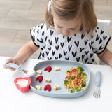 A young child enjoys spaghetti, cheese, and raspberries using Bumkins Spoon + Fork: Gray on a gray plate in a white high chair.