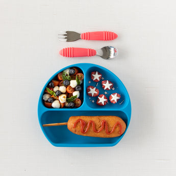 Kids meal with a corn dog, decorated cucumber, blueberries, yogurt with star sprinkles & Bumkins red spoon + fork set.