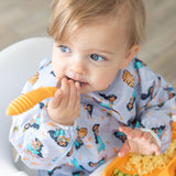 Close-up of a child in a pastel bib holding a Bumkins Spoon + Fork: Tangerine.