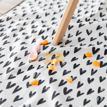 Close-up of a spoon and squashed orange pieces on a Bumkins Splat Mat: Hearts underneath a high chair.