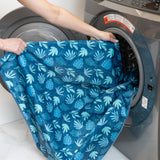 A person puts the waterproof Splat Mat: Blue Tropic by Bumkins into a front-load washer for easy cleaning.