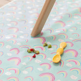 A yellow spoon from Bumkins Silicone Dipping Spoons 3 Pack: Tutti-Frutti lays on a rainbow patterned mat next to bits of fruit.