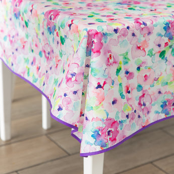 Bumkins Splat Mat: Watercolor in pink, purple, blue, and green hues with a purple trim drapes over a white table.