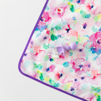 A Bumkins Silicone Chewtensils®: Lavender lays on top of a floral mat with yogurt splatter on a white background.