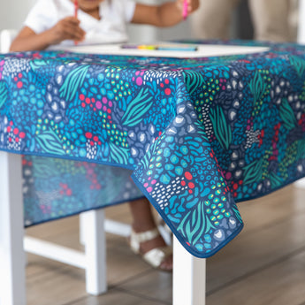 A child coloring at a table with a Bumkins Splat Mat: Animal Prints draped over the top.