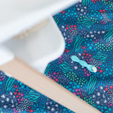 A silicone spoon with food rests on a Bumkins Splat Mat: Animal Prints underneath a high chair.