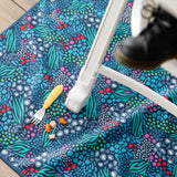Bumkins Splat Mat: Animal Prints lays under a high chair, with a yellow fork and pieces of food on top.
