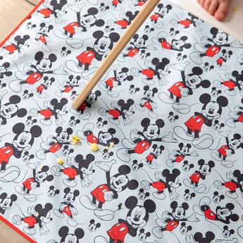 A broom sweeps crumbs off a machine washable Splat Mat: Mickey Mouse by Bumkins.