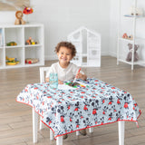 Child painting on a Bumkins Splat Mat: Mickey Mouse, at a table in a bright room with toys on shelves.
