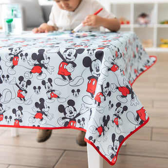 A child draws on paper at a table with a Bumkins Splat Mat featuring Mickey Mouse in his iconic red shorts.
