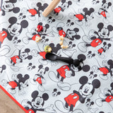 Bumkins Mickey Mouse Splat Mat features scattered food, a black spoon, and rolling pin on waterproof fabric. Machine washable for easy cleanup.