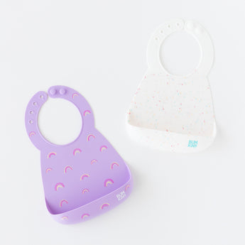 Bumkins Silicone Bib 2 Pack: Vanilla Sprinkle and Rainbows lays flat on a white background.