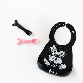 Bumkins Silicone Dipping Spoons: Minnie Mouse (Black and Pink) lay next to a black bib with a Mickey & Minnie design on a white background.