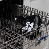 A bib from Bumkins Silicone Bib 2 Pack: Disney Mickey and Minnie Mouse sits in the top rack of an open dishwasher.