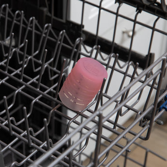 A cup from Bumkins First Foods Deluxe 6-Piece Mealtime Set: Pink Jelly sits in the top rack of an open dishwasher.