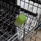 A cup from Bumkins First Foods Deluxe 6-Piece Mealtime Set: Green Jelly sits in the top rack of an open dishwasher.