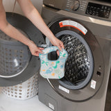 Placing a colorful Bumkins Starter Bib 2 Pack: Dinosaurs & Blue Tropic, made of waterproof fabric, into a front-load washer.