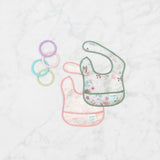 Bumkins Starter Bib 2 Pack: Floral & Lace  lays overlapped on a marble background with 4 pastel teething rings nearby.