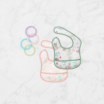 Bumkins Starter Bib 2 Pack: Floral & Lace  lays overlapped on a marble background with 4 pastel teething rings nearby.