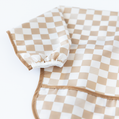 Close-up of a tan checkered sleeved bib on a white background, with focus on the folded over sleeve.