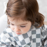 Close-up of a young girl in a bib from Bumkins On-The-Go Mealtime 6-Piece Set: Charcoal Check + Grey.