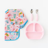 A Bumkins Sleeved Bib 2 Pack: Disco Boots lays folded next to a pink divided plate and matching utensils on a white background.