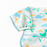 Close-up of Bumkins Sleeved Bib: Dinosaurs on a white background with focus on the elastic cuff on the sleeve.