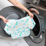 A person holds a bib from Bumkins SuperBib® and Sleeved Bib 3-Piece Set: Hangry, Dinosaurs, Blue Tropics in front of an open washing machine.