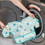 A person holds a bib from Bumkins SuperBib® and Sleeved Bib 3-Piece Set: Rolling With The Waves, Whale Tail, Ocean Life in front of a washer.