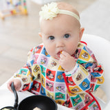 A baby in a bow wearing a bib from Bumkins Sleeved Bib 2 Pack: Mickey & Friends Excellent Eight eats from a bowl with a spoon in a high chair.